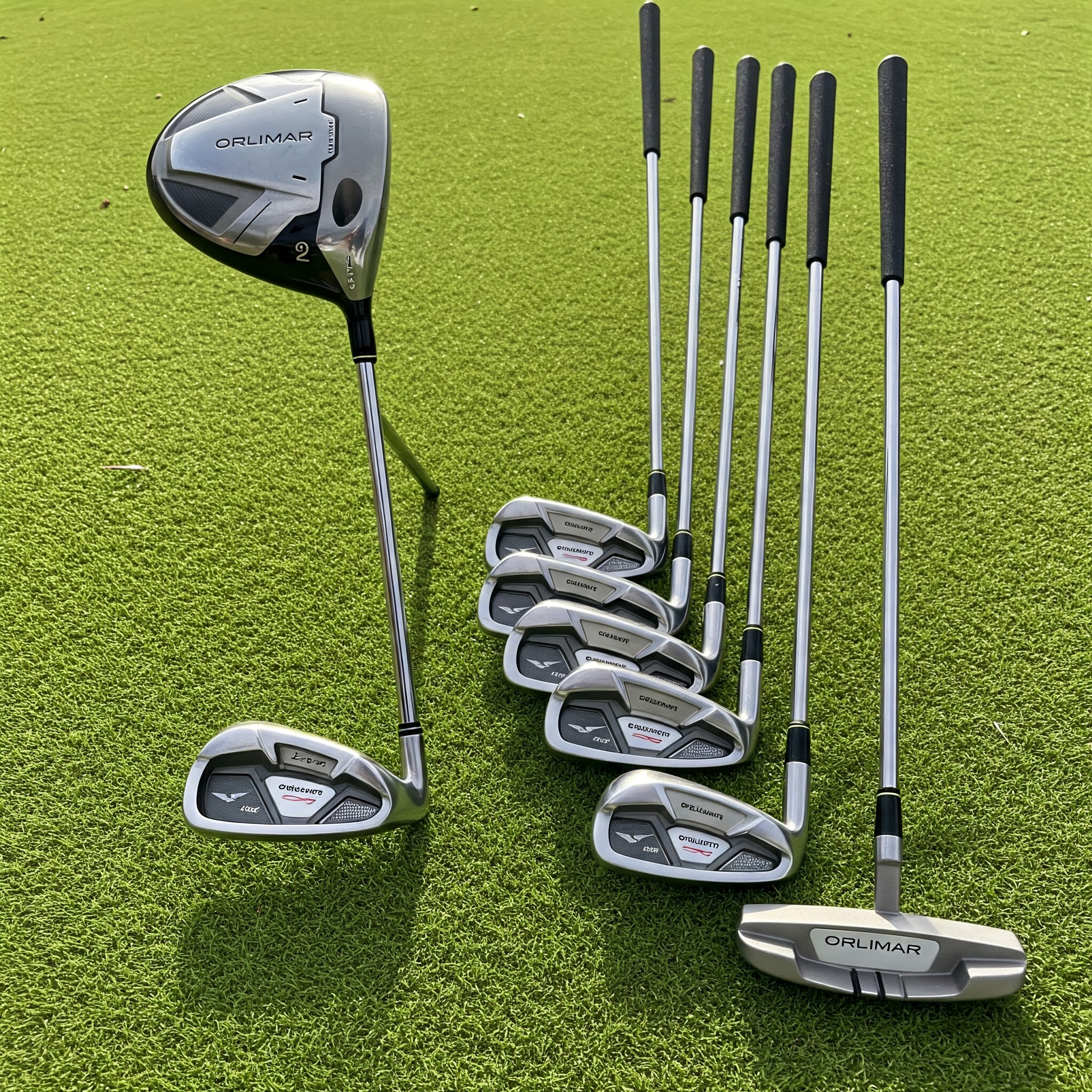 A complete set of Orlimar Golf Clubs, including driver, irons, and putter, displayed on a green grass background.
